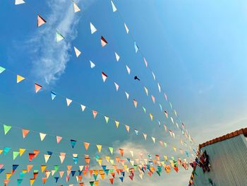 Low angle view of multi colored flags hanging against blue sky