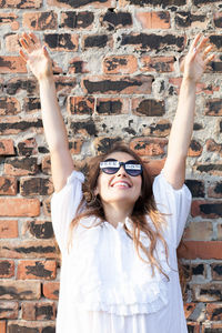 Smiling woman wearing freedom text sunglasses against brick wall