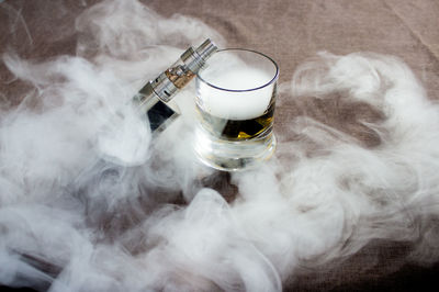 Glass and electronic cigarette amidst smoke on table