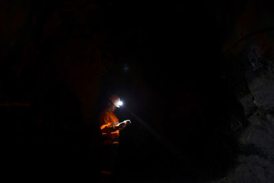 Man with illuminated headlamp in dark cave