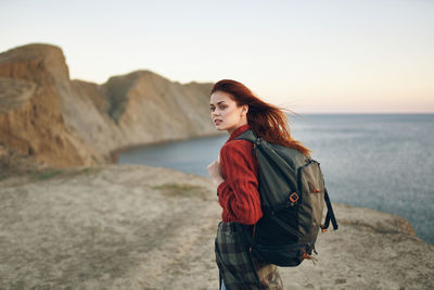 Young woman standing by sea against sky during sunset