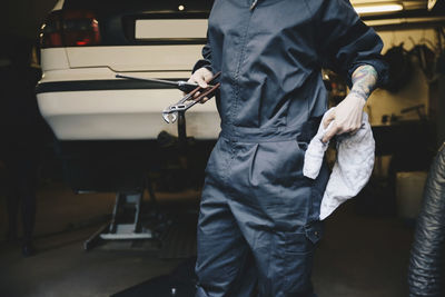 Midsection of female mechanic holding napkin and work tools at auto repair shop