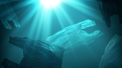 Creative background of single-use plastic bags floating in sea or ocean with sunlight effect