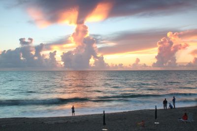 People on beach against sky during sunset