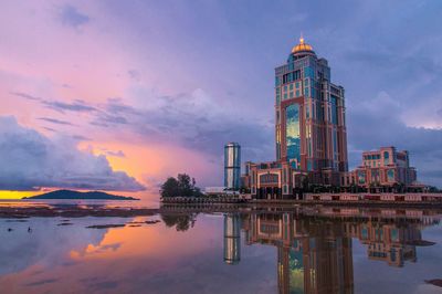 Reflection of buildings in lake against sky during sunset