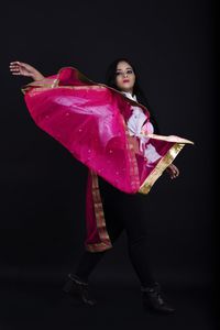 Portrait of young woman standing against pink background