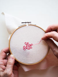 Close-up of the hand of an adult woman who embroiders the word love on a white background
