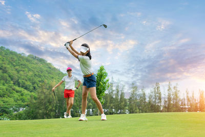 Full length of man with arms raised standing on golf course against cloudy sky