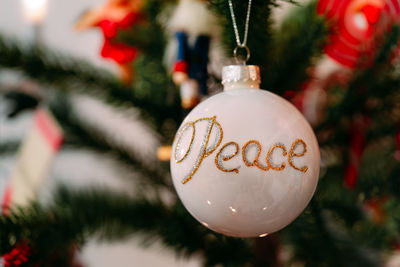 Close-up of christmas decoration with peace text hanging on tree