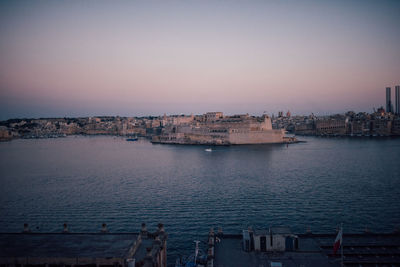 Buildings by sea against clear sky at sunset