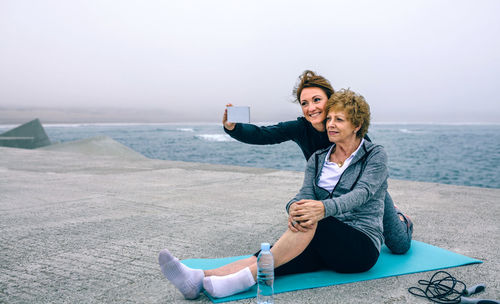 Mother and daughter taking selfie at beach against sky