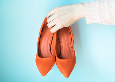 Close-up of woman hand holding shoes against blue background