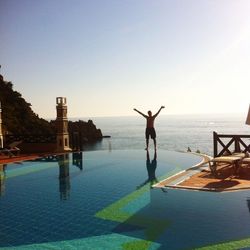 Rear view of person standing at swimming pool against sky