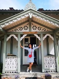 Full length of young woman standing against house