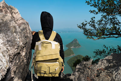 Rear view of woman with backpack looking at view while standing by rock formations against sea and sky