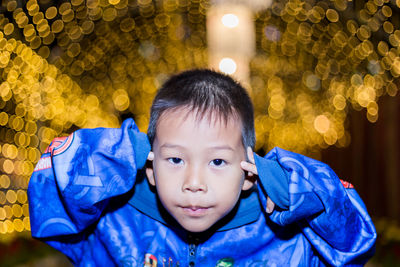 Portrait of cute boy in blue jacket against illuminated lights