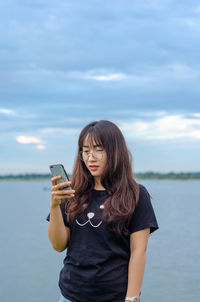 Young woman using smart phone against sky