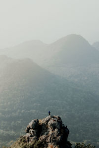 Distant view of boy standing on cliff against landscape