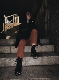 Full length of woman sitting on staircase against wall