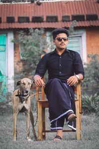 Full length of young man sitting on chair with dog outdoors