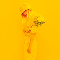 Close-up of woman holding bouquet against yellow background