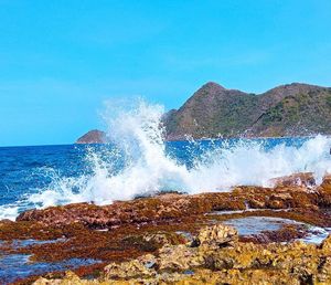 Waves splashing on rocks against clear blue sky