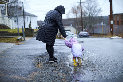 A mother and child having fun splashing in puddles on a rainy day.