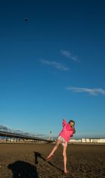 Rear view of girl playing at beach against blue sky