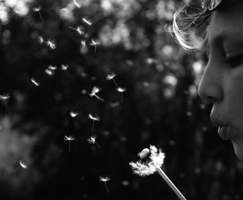 Close-up of woman blowing dandelion seeds at park