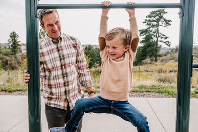 Young boy hanging on a bar at a park outside