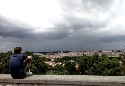 Rear view of man sitting on city against sky