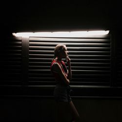 Young woman standing against illuminated light at night