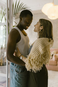 Side view of smiling multiracial young couple standing with each other at home