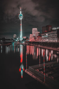 Illuminated buildings by river against sky in city at night