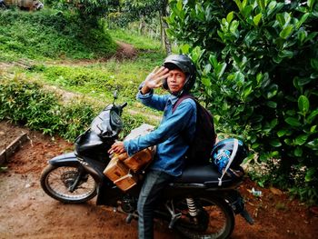 Portrait of smiling man gesturing while sitting on motorcycle against plants