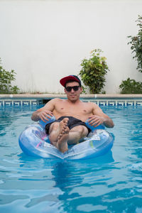 Portrait of shirtless young man relaxing on pool raft in swimming pool