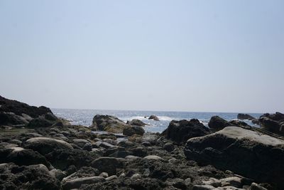 Scenic view of sea in front of rocks against clear sky on sunny day