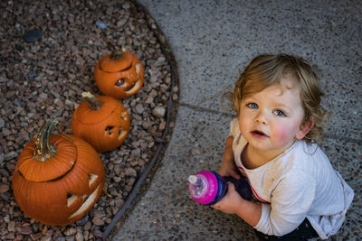 High angle view portrait of girl crouching by pumpkin