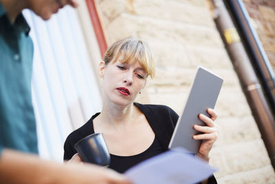 Mid adult businesswoman holding digital tablet and coffee cup while discussing with colleague outside office