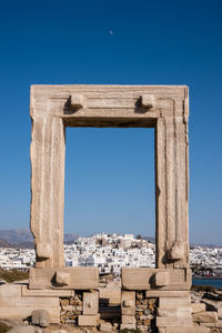 Ancient portal portara of naxos against city skyline and clear blue sky