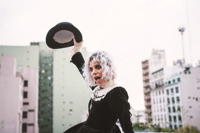 Woman with hat standing against buildings in city