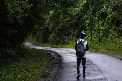 Rear view of man with backpack walking on road amidst trees in forest