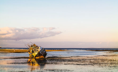 Abandoned boat on beach against sky during sunset