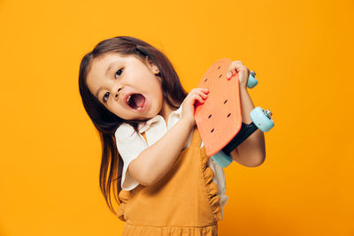 Portrait of cute girl holding toy against yellow background