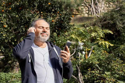 Handsome smiling mature man having video call or listening to music with cellphone and hadphones. 