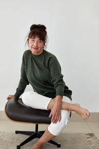 Portrait of woman sitting on chair against wall