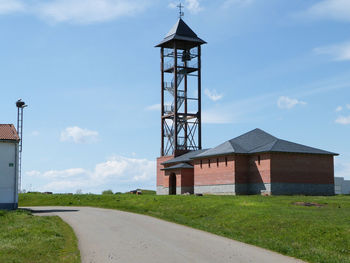 Road by bell tower and church on grassy field against sky