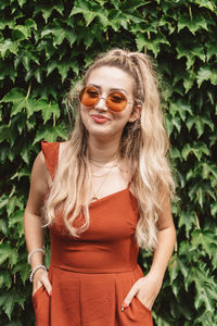 Young woman wearing sunglasses standing against plants