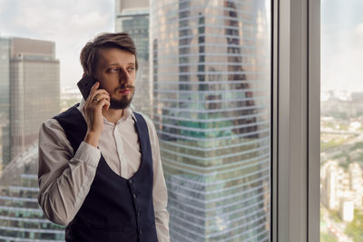 Businessman with beard is talking
on the phone in a skyscraper apartment in the afternoon in summer