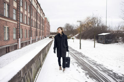 Young man with suitcase walking along snowy sidewalk